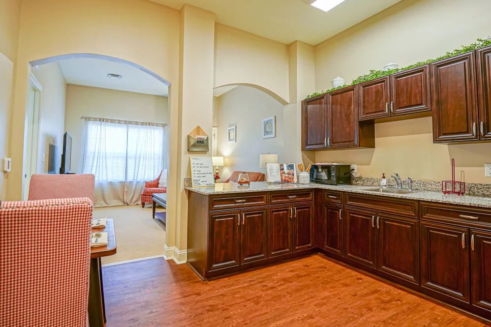 A cozy kitchen with wooden cabinets and modern appliances, featuring an open layout leading to a well-lit living area.