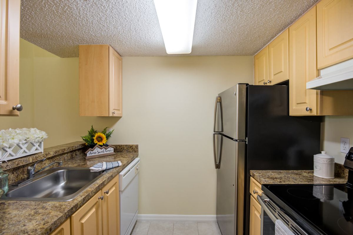 A modern kitchen with light wood cabinets, a stainless steel refrigerator, and granite countertops.