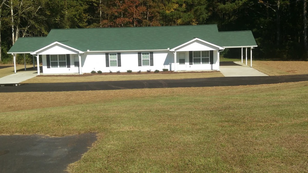 A single-story house with a green roof and a large lawn.