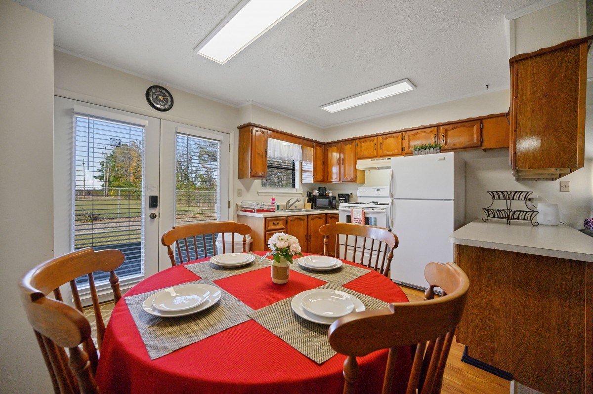 A cozy kitchen with a dining table set for four, featuring a red tablecloth and wooden chairs.