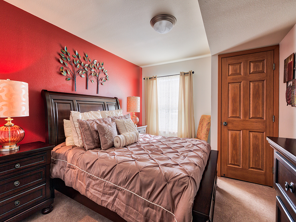 A cozy bedroom with a warm red accent wall, stylish bedding, and natural light streaming through the window.