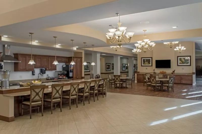 A spacious dining area with a kitchen, chandeliers, and ample seating.