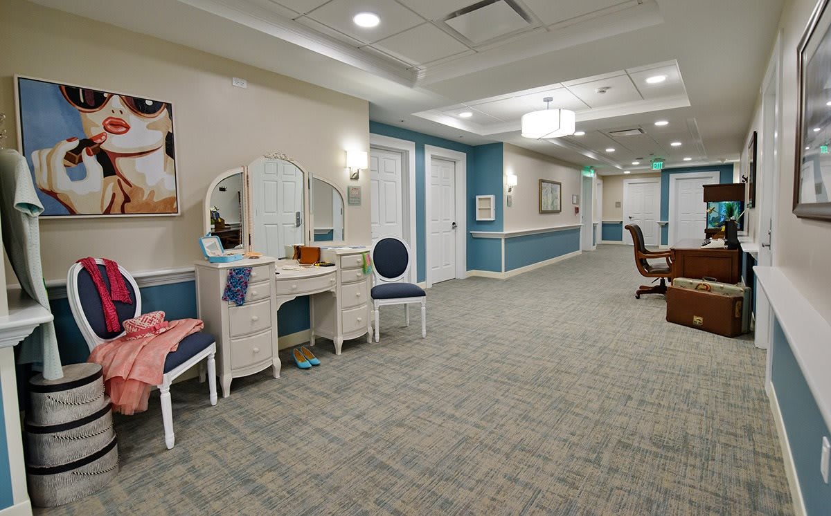 A well-lit hallway featuring a dressing table and chairs with carpeted flooring.