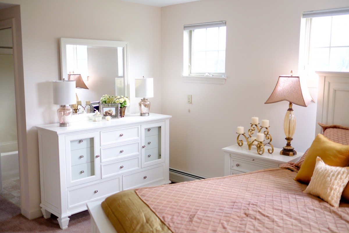 A cozy bedroom with a white dresser, mirror, and lamp.