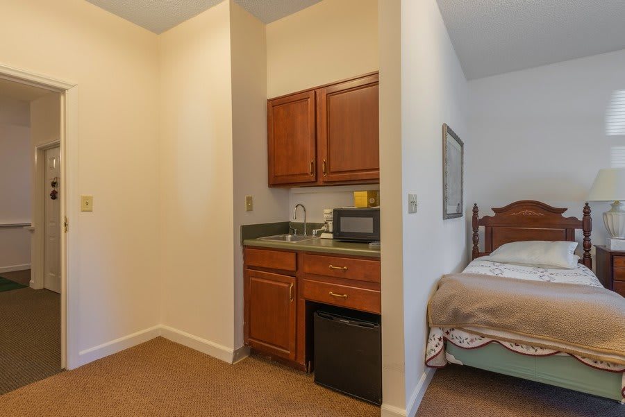 A hotel room featuring a small kitchenette with cabinets, a sink, a microwave, and a mini fridge adjacent to the sleeping area.