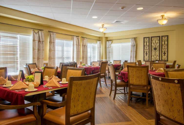 A cozy dining room with neatly arranged tables and chairs, featuring large windows and inviting decor.