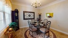 A stylish dining room featuring a round glass table with ornate chairs, complemented by a chandelier and decorative artwork.