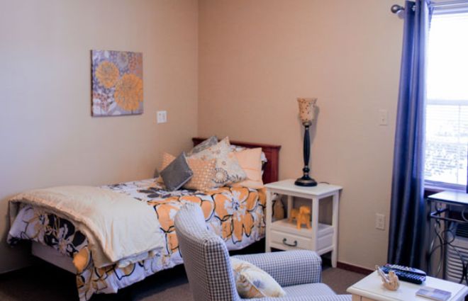 A cozy bedroom with a single bed adorned with floral bedding, a nightstand with a lamp, and decorative elements creating a warm atmosphere.
