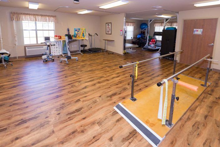 A therapy room equipped with parallel bars and various exercise equipment for rehabilitation exercises.