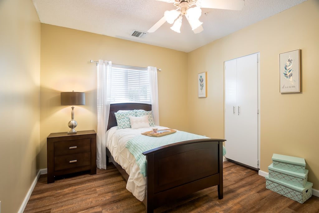 A cozy bedroom with a single bed, nightstand, and ceiling fan.