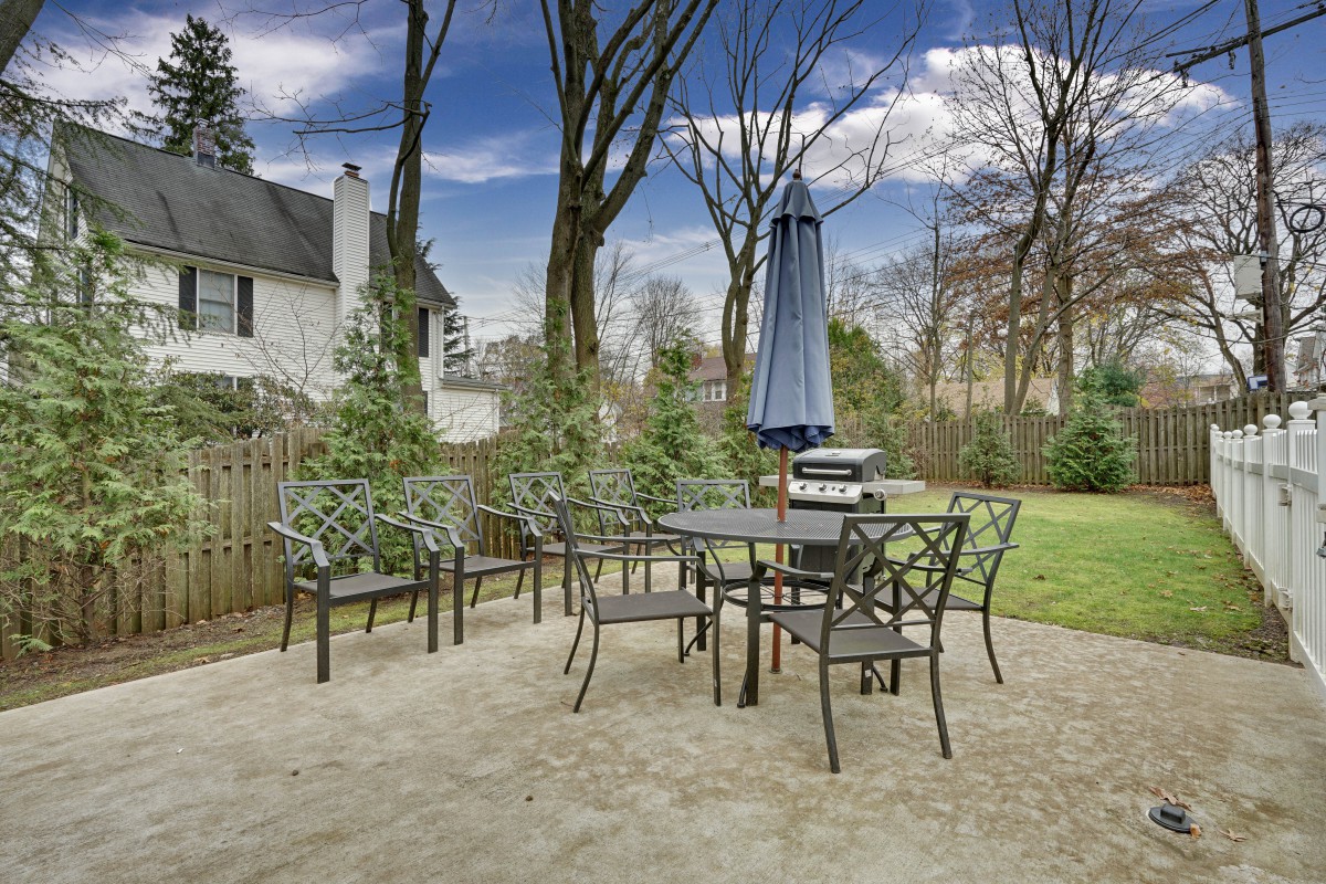 A backyard patio with a set of metal furniture including a table, chairs, and an umbrella.