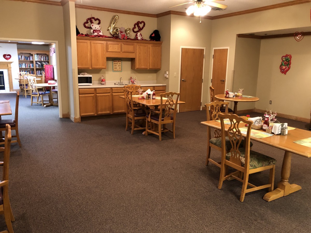 A cozy dining area with wooden tables and chairs, adjacent to a small kitchen space.