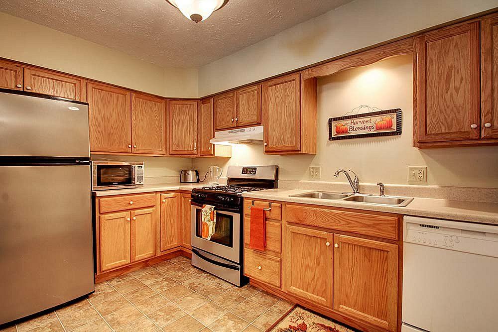 A modern kitchen with wooden cabinets, stainless steel appliances, and tile flooring.