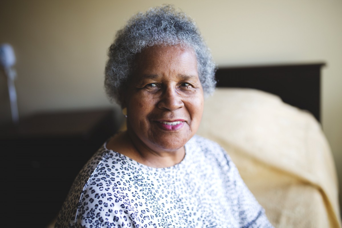 An older adult smiling while sitting indoors.