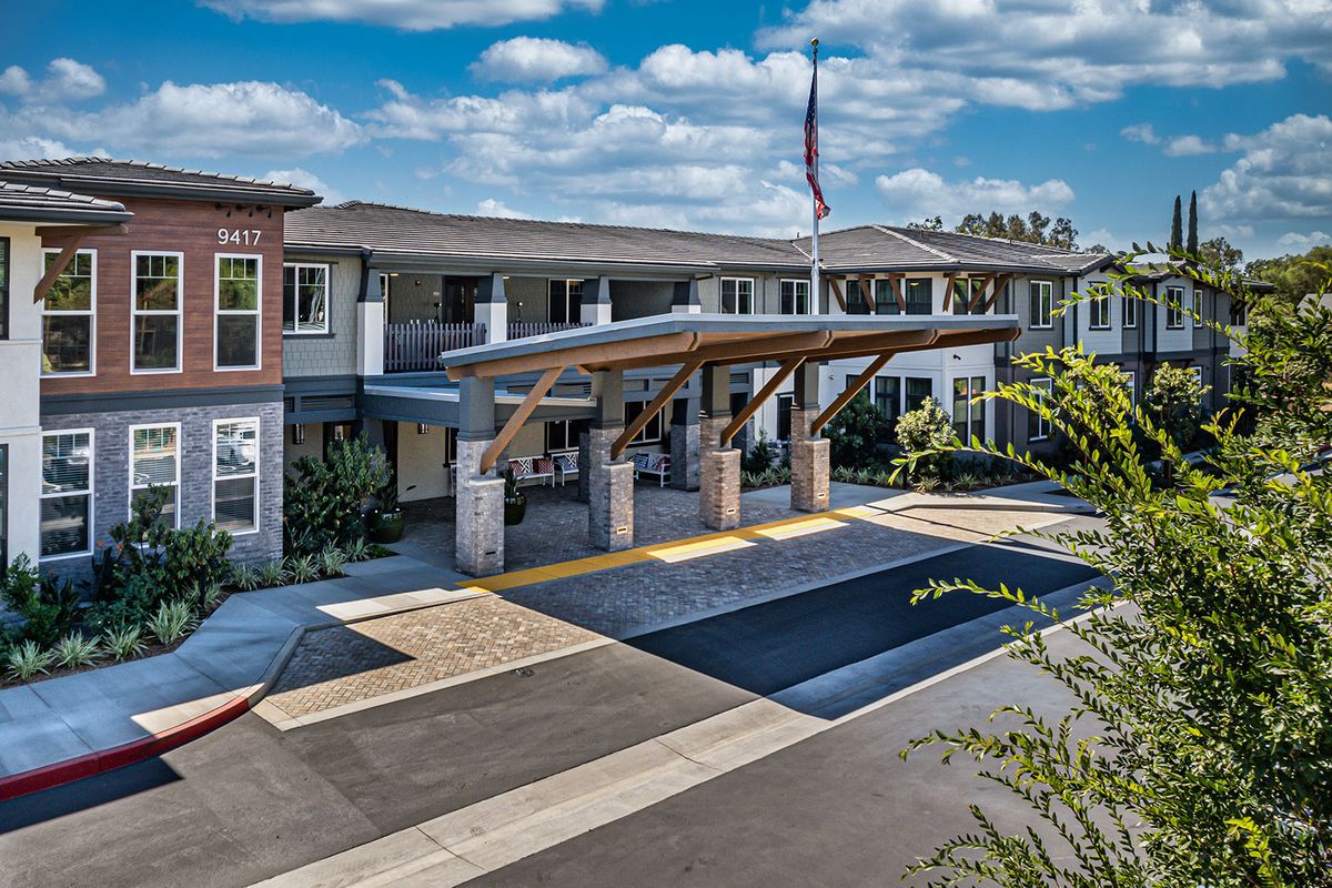 A modern building with a prominent entrance and flag, set against a backdrop of blue sky and clouds.