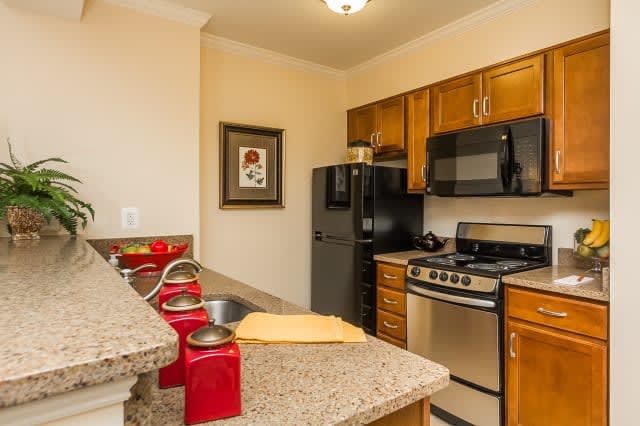 A modern kitchen with wood cabinets and a granite countertop, featuring appliances like a refrigerator, stove, and microwave.
