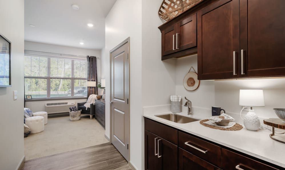 A modern interior featuring a small kitchen area with dark wooden cabinets and a living space in the background.