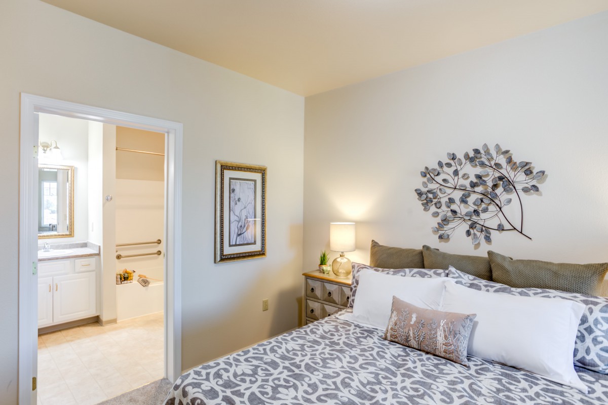 A cozy bedroom featuring a bed with patterned bedding, a nightstand with a lamp, and decorative artwork on the wall.