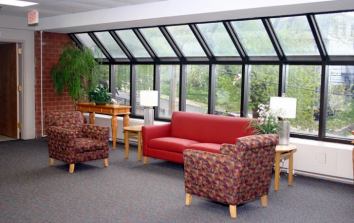 A cozy lounge area with a red sofa, patterned chairs, and large windows overlooking greenery.