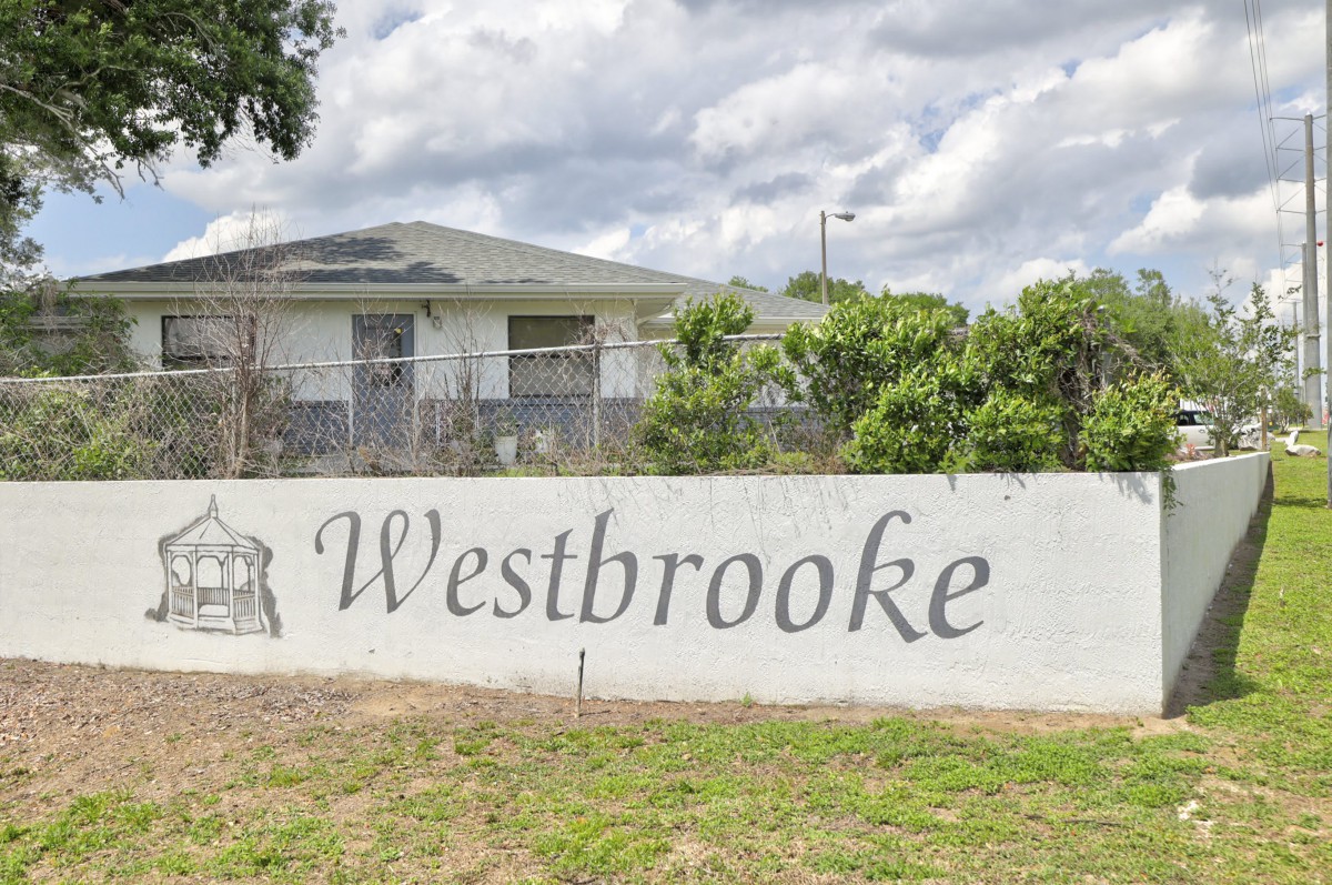 A sign for Westbrooke in front of a fenced building with a cloudy sky above.