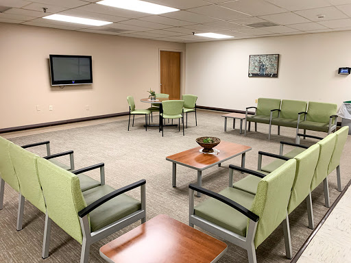 A modern and inviting waiting room with green chairs and wooden tables.
