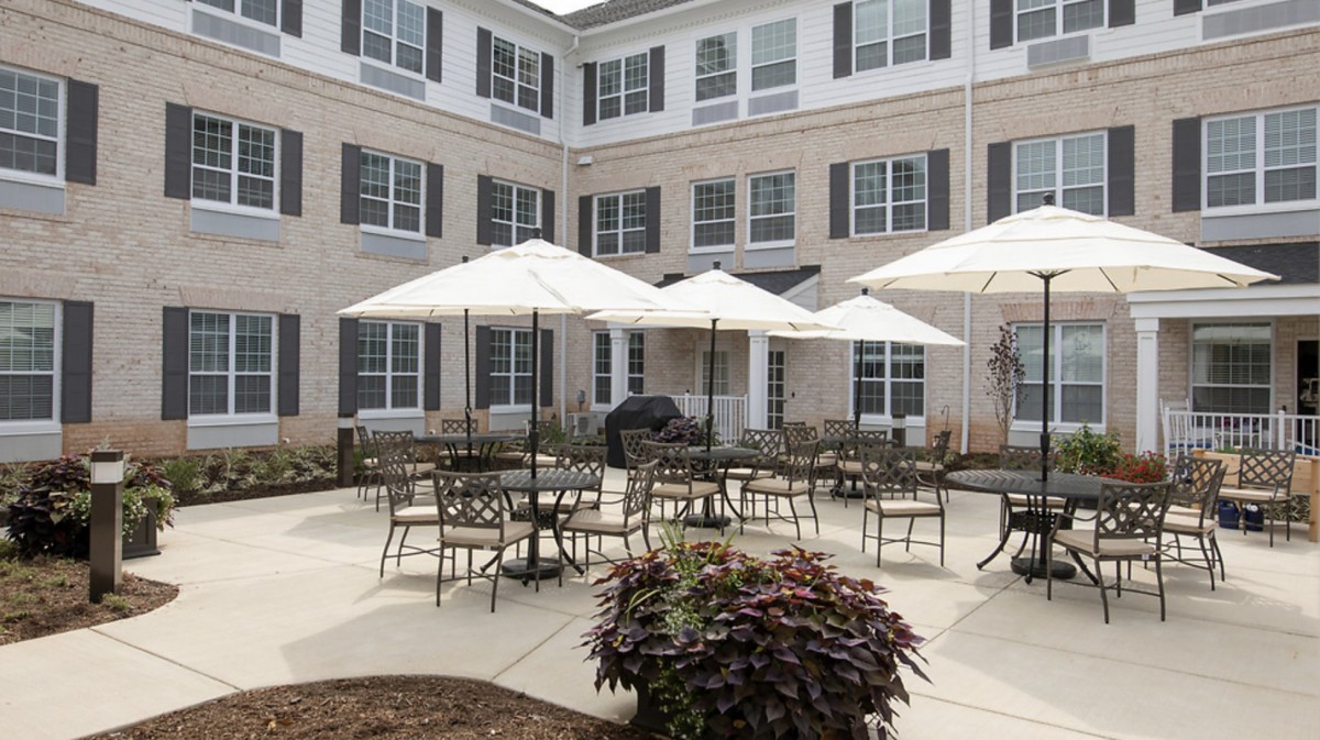 A spacious outdoor patio area with tables, chairs, and umbrellas in front of a multi-story building.