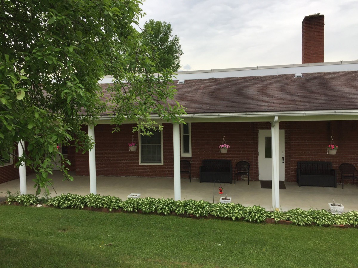 A brick house with a covered patio and a well-maintained lawn.