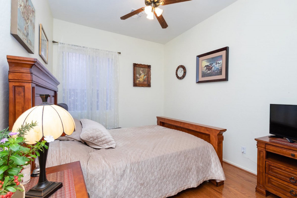A cozy bedroom with a bed, ceiling fan, and artwork on the walls.