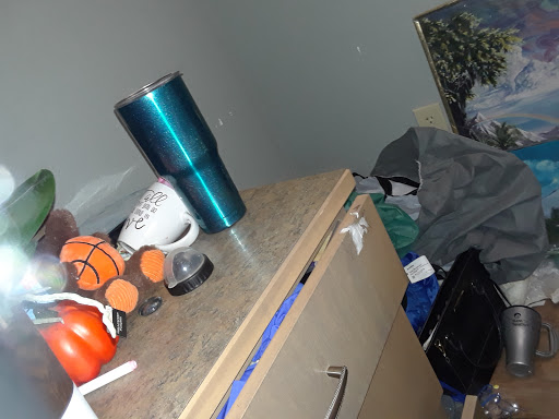 A cluttered tabletop featuring various items including a coffee mug, a water bottle, and scattered clothing.