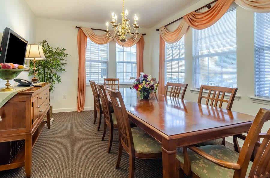 A well-furnished dining room with a large table, chairs, chandelier, and elegant curtains.