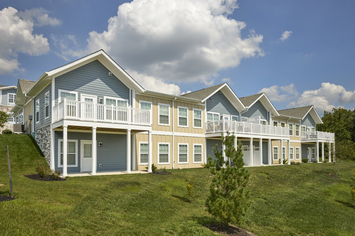 A suburban apartment complex with multiple units and a grassy lawn under a partly cloudy sky.