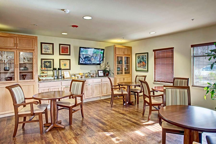 A cozy indoor seating area with wooden floors, several tables and chairs, decorated walls, and a television.