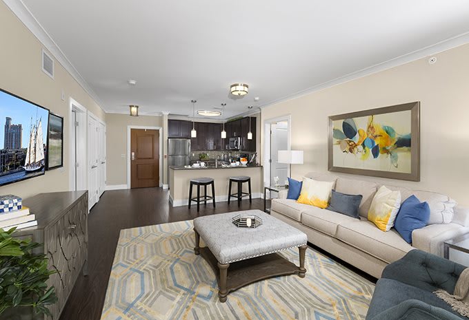A modern living room with a comfortable sofa and a view into the kitchen area, featuring stylish decor and contemporary artwork.