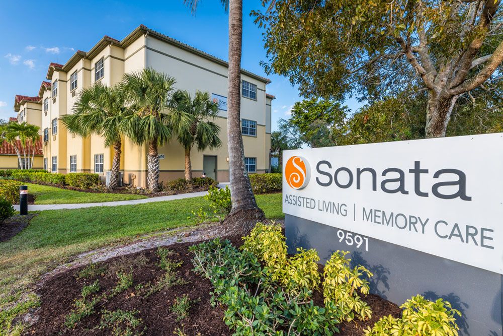 A sunny day view of Sonata building with a sign in the foreground surrounded by lush landscaping and palm trees.