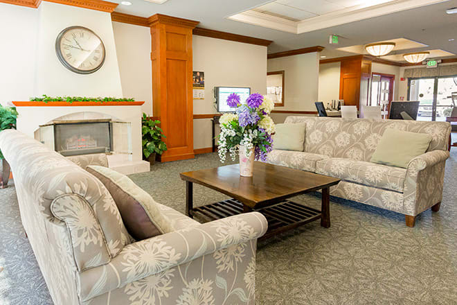 A cozy living room with patterned sofas, a wooden coffee table with a floral arrangement, and a fireplace.