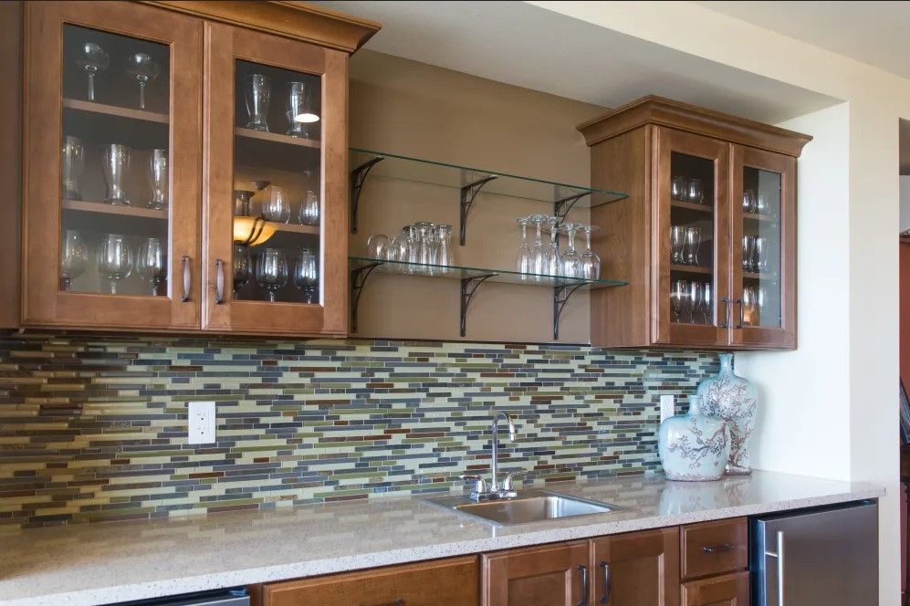 Modern kitchen with wooden cabinets, glass shelves, and a colorful tile backsplash.