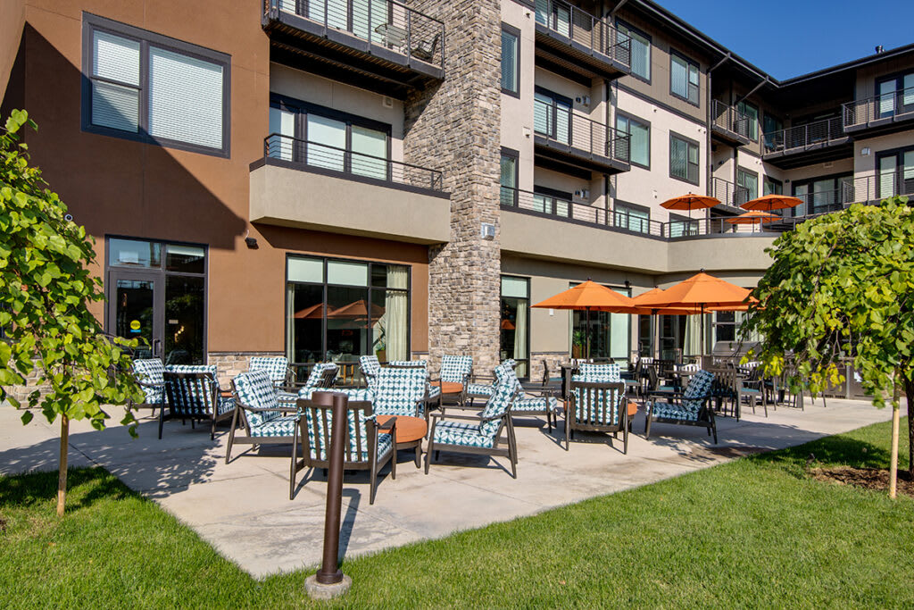 A modern apartment building with a spacious patio area featuring outdoor seating and bright umbrellas.