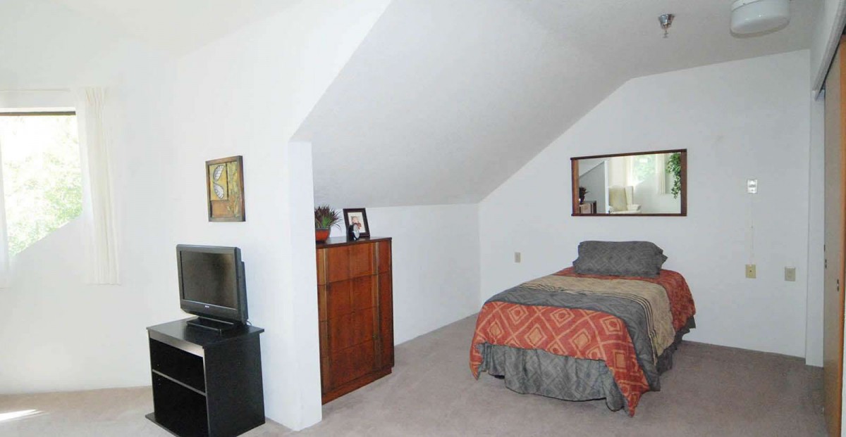 A cozy attic bedroom with a bed, dresser, and slanted ceiling.