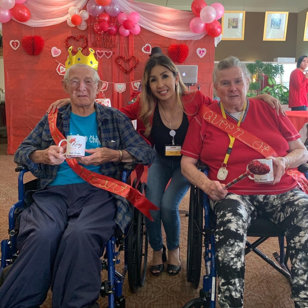 A heartwarming community celebration with two elderly individuals in wheelchairs, wearing crowns, joined by a smiling woman.