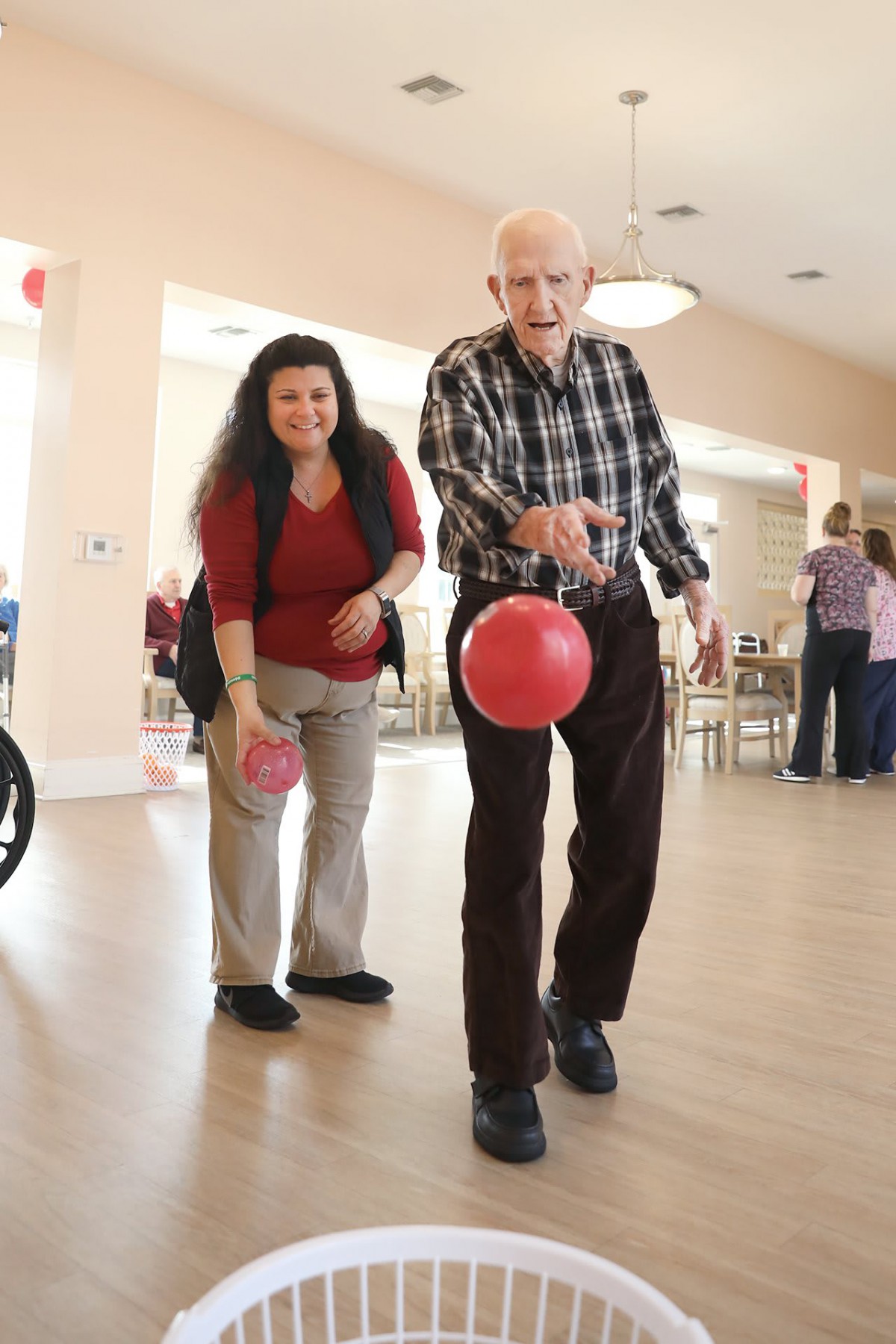 An elderly man enjoying a game of indoor bowling with assistance.