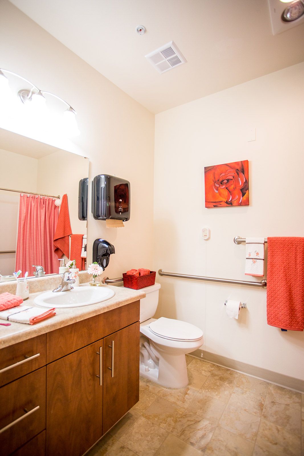 A bright bathroom featuring orange accents with a sink, toilet, and mirror.