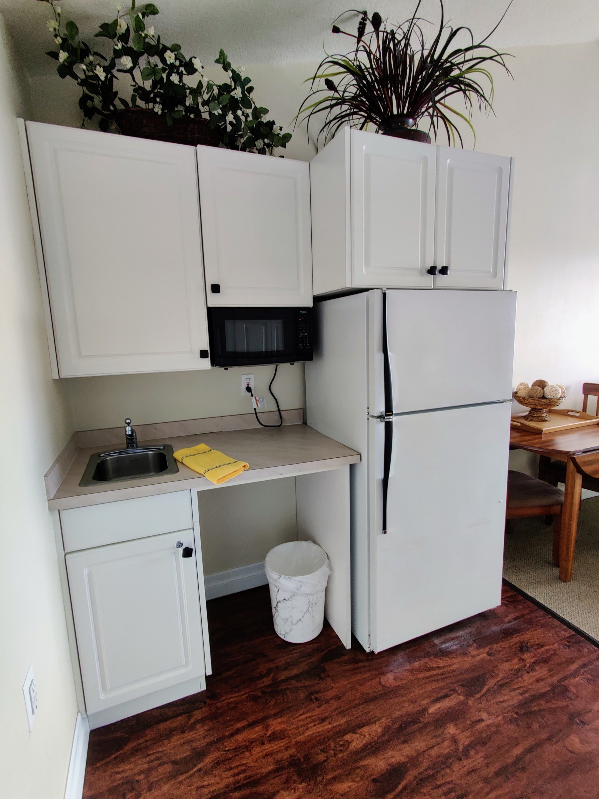 A compact kitchen with white cabinets, a refrigerator, microwave, and sink.