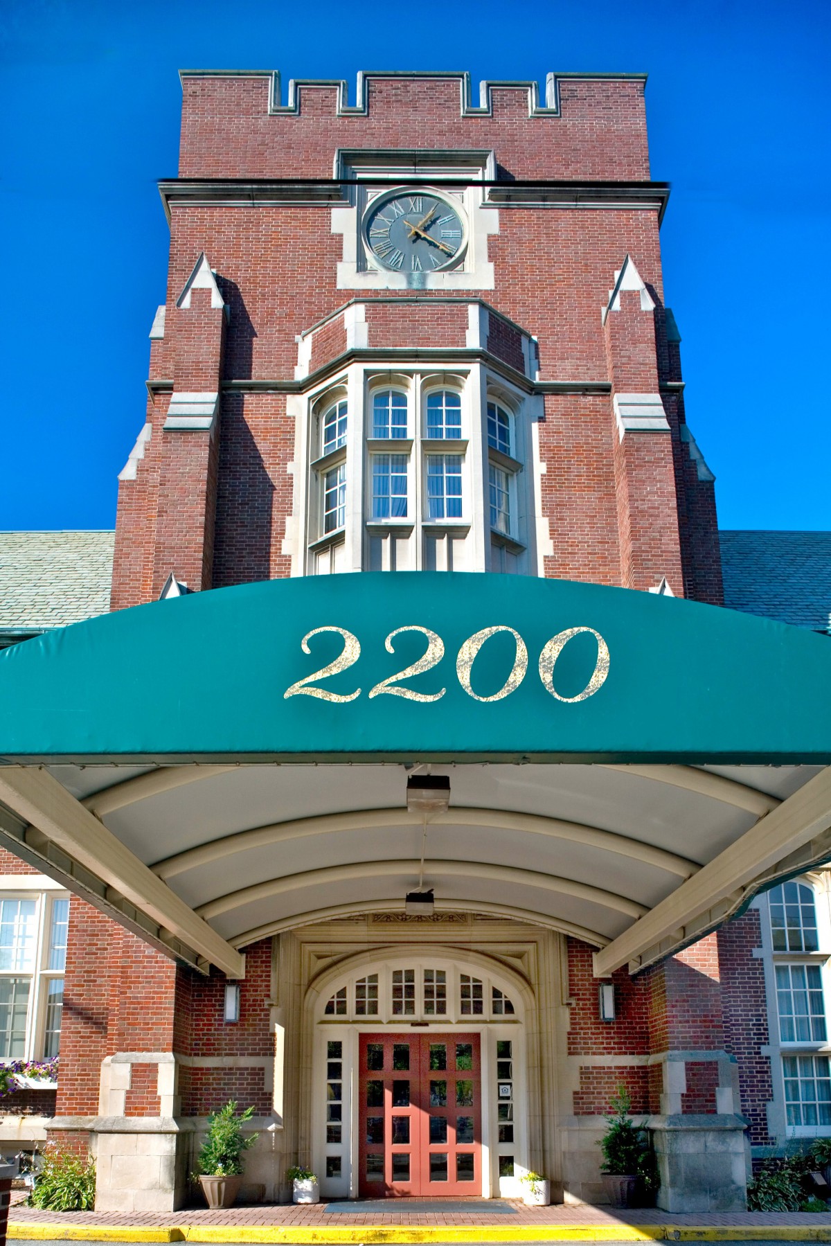 A brick building with a green awning displaying the number 2200, featuring an ornate entrance and a clock tower.