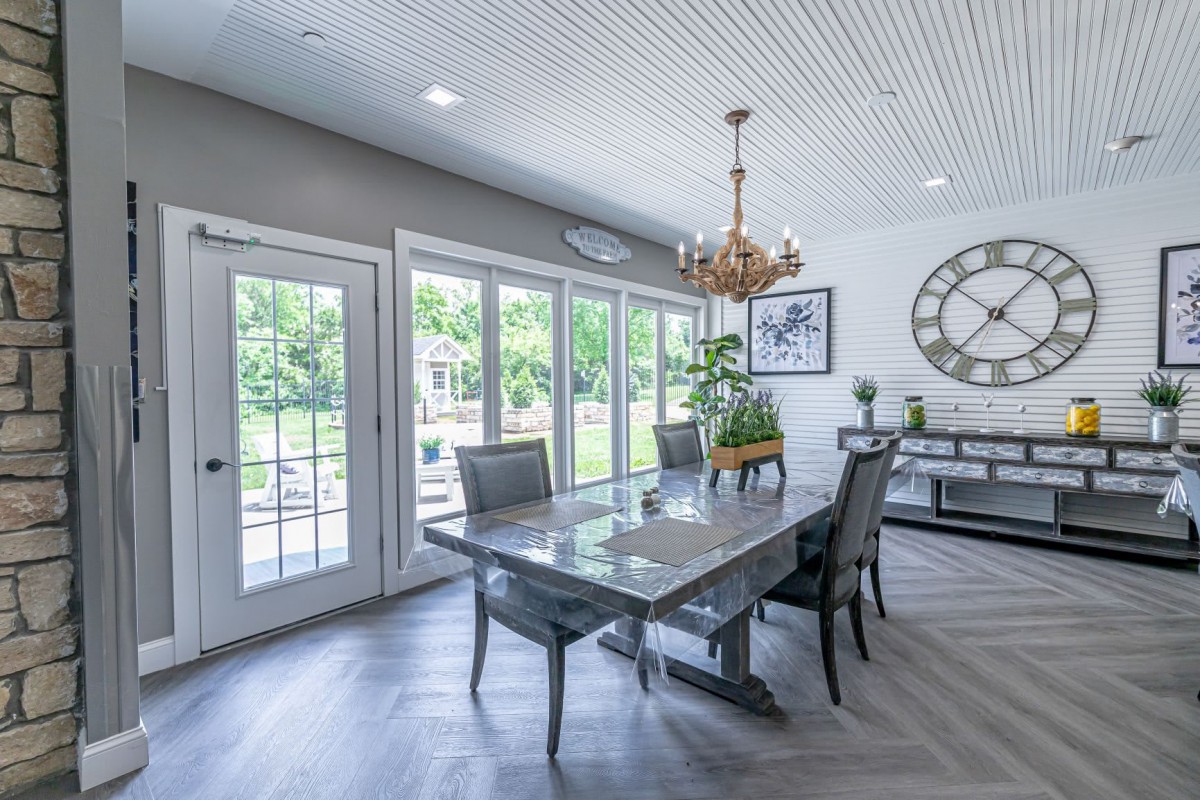 A modern dining room with a large table, stylish chairs, and a chandelier, featuring ample natural light through French doors.