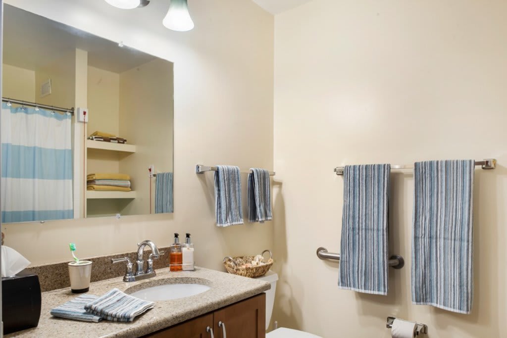 A neatly organized bathroom with blue striped towels and wooden cabinets.