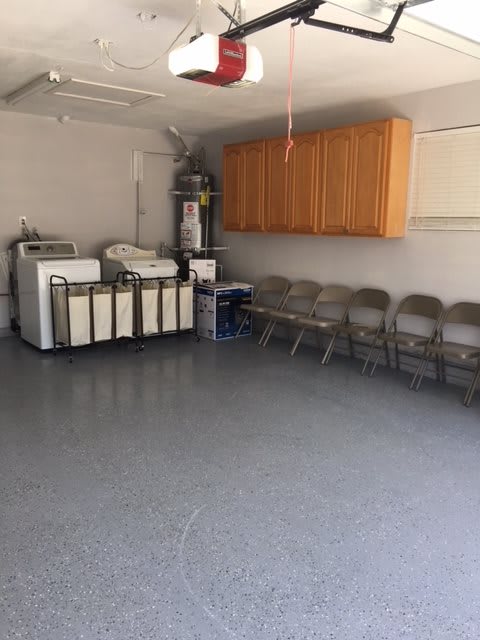 A clean garage with washing machines, dryers, folding chairs, and wooden cabinets.