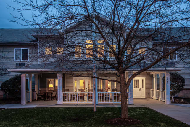 A cozy house with its lights on in the evening, featuring a front porch and tree in the yard.