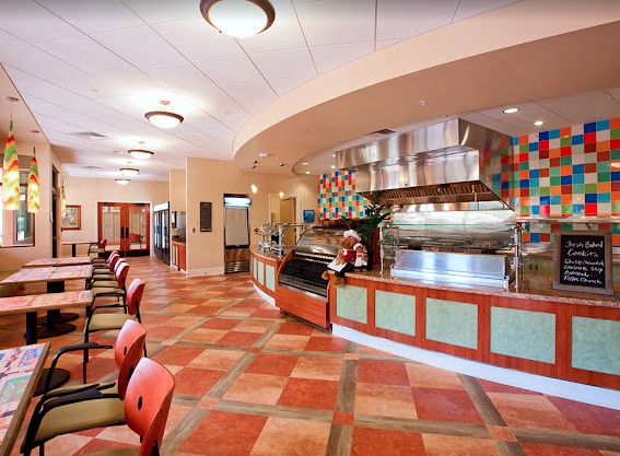 A modern restaurant interior with a dining area, featuring colorful tile flooring and stylish lighting fixtures.