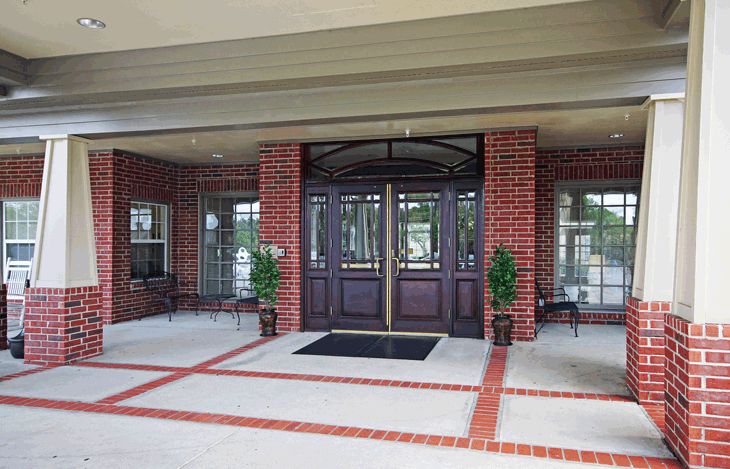 The entrance of a brick building with double doors and potted plants on either side.