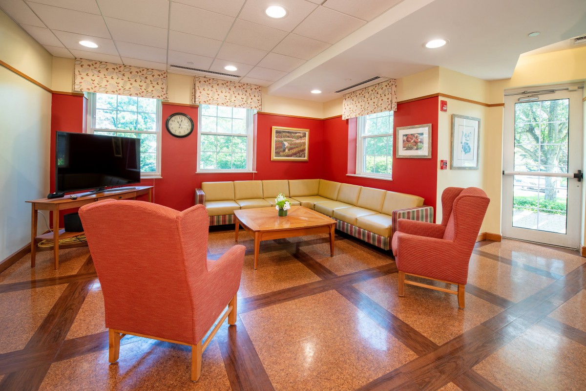 A cozy living room with red walls, featuring a couch, armchairs, and a wooden coffee table.